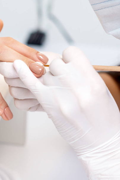 Manicure master in guanti protettivi applicando smalto beige sulle unghie femminili nel salone di bellezza - Foto, immagini