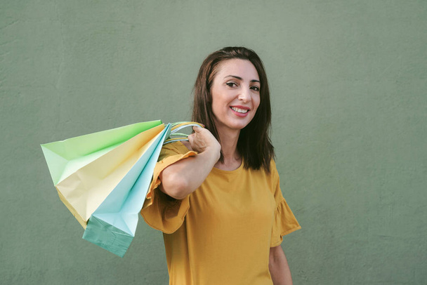 mosolygós fiatal nő gazdaság bevásárló táskák át zöld háttér - Fotó, kép