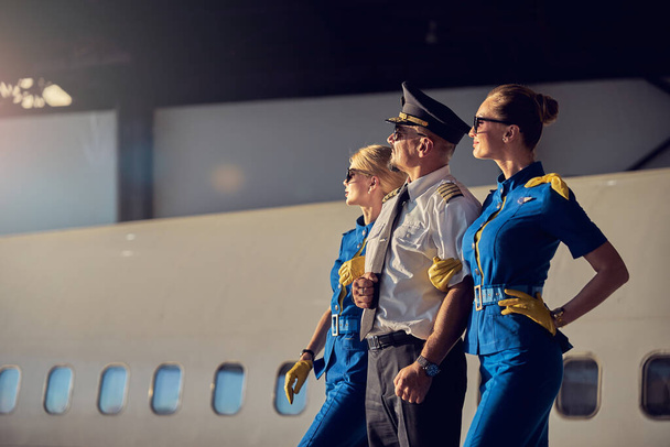 Elegant charming women flight stewardesses with captain of aircraft standing in aviation hangar - Foto, Bild