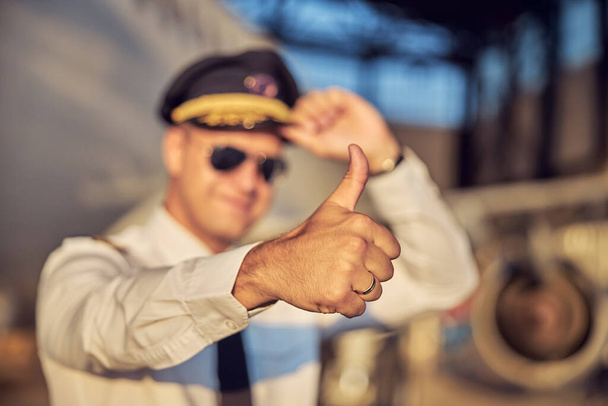 Уверенный капитан воздушного судна в шляпе и белой рубашке позирует перед фотокамерой - Фото, изображение