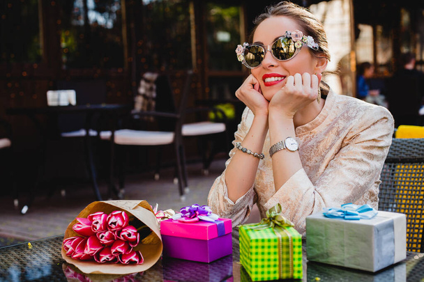 young stylish beautiful woman in fashion sunglasses sitting at cafe, elegant, smiling and happy, enjoying warm day, presents, tulips, happy birthday party, city street, europe vacation - Fotó, kép