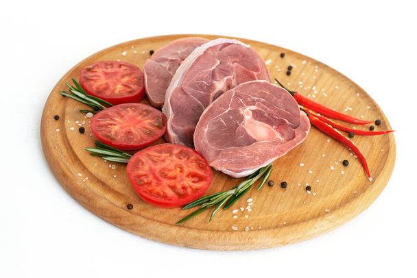 pieces of raw turkey meat, chopped leg steak, portioned barbecue pieces, on a round wooden board and and a white background with a sprig of rosemary, tomatoes and red hot pepper. isolate... - Photo, Image