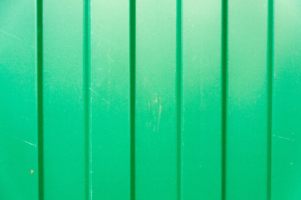 Cerca de perfil de metal verde com um padrão de linhas verticais ou tiras com uma estrutura escalonada e uma textura convexa ou fundo. Fechar macro - Foto, Imagem