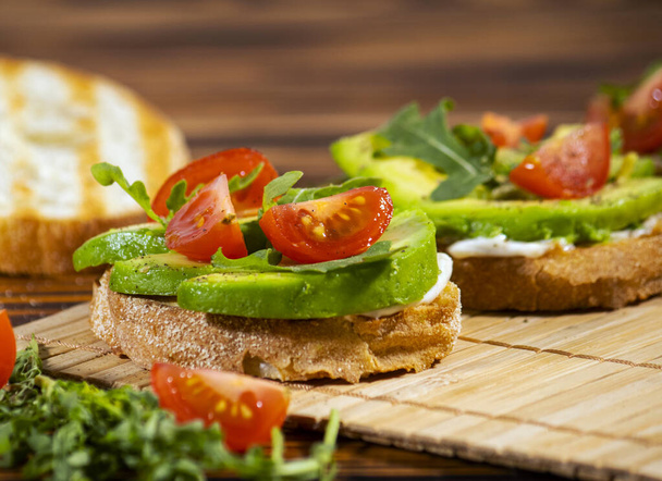 Avocado puree en verse gesneden tomaten op gegrild toast brood op bruine houten achtergrond. Trendy en gezond ontbijt. Gezond en heerlijk eten. - Foto, afbeelding