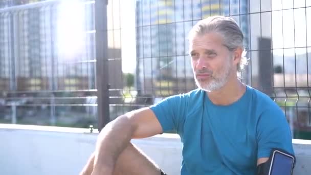 Modern man in sportswear taking a break after jogging or exercise in urban area - Footage, Video