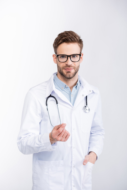 Positive ophthalmologist with hand in pocket wearing eyeglasses and looking at camera isolated on white - Fotó, kép