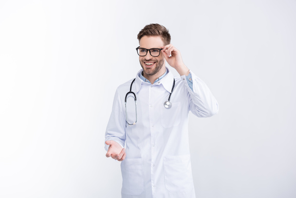 Happy doctor with stethoscope, holding eyeglasses frame, gesturing isolated on white - Fotografie, Obrázek