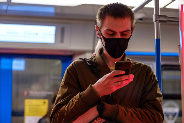 Moscow. Russia. September 28, 2020 A man in a subway car is looking at his smartphone with enthusiasm. The passenger has a protective medical mask on the face. Second wave of coronavirus. - Photo, image