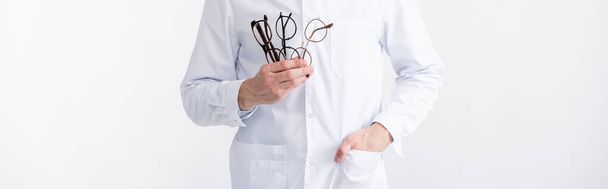Przycięty widok lekarza z ręką w kieszeni trzymając kilka okularów izolowanych na białym, baner - Zdjęcie, obraz
