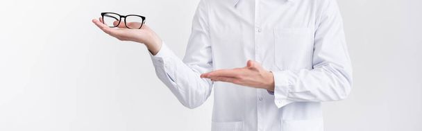 Cropped view of ophthalmologist holding and pointing with hand at eyeglasses on palm isolated on white, banner - Valokuva, kuva