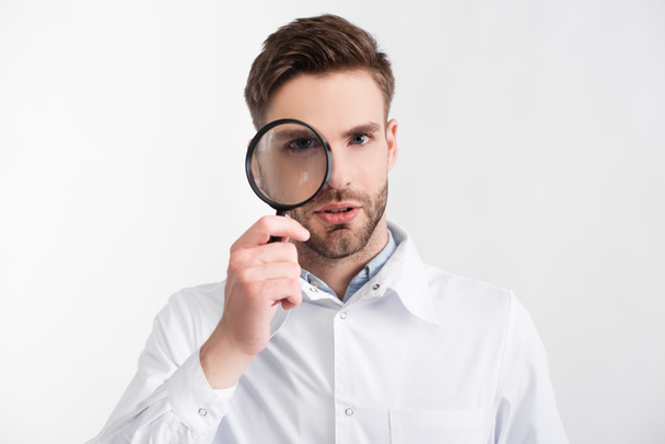 Portrait of confident ophthalmologist looking through loupe isolated on white - Fotó, kép