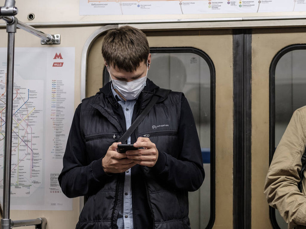 Moscow. Russia. September 28, 2020 A man in a subway car is looking at his smartphone with enthusiasm. The passenger has a protective medical mask on the face. Second wave of coronavirus. - Photo, image