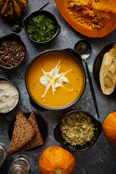 Delicious pumpkin soup with cream, seeds, bread and fresh herbs in elegant ceramic black bowl - Foto, afbeelding