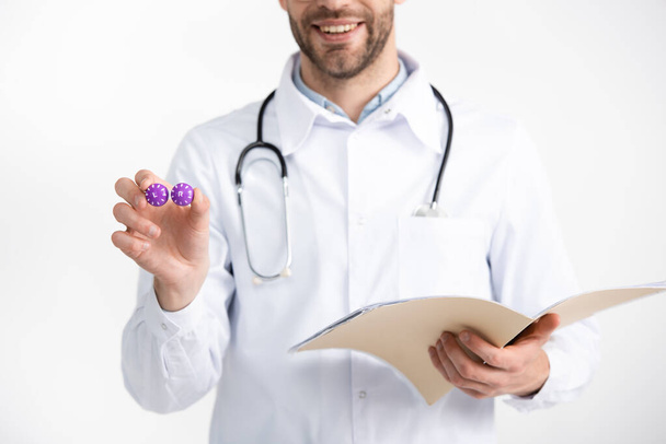 Ausgeschnittene Ansicht eines lächelnden Augenarztes mit Stethoskop, das Folder und Linsenbehälter auf weiß isoliert hält - Foto, Bild