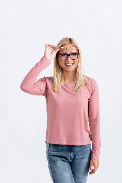 Χαμογελαστή ξανθιά γυναίκα που κρατάει γυαλιά ενώ κοιτάζει την κάμερα απομονωμένη στο γκρι - Φωτογραφία, εικόνα