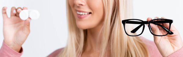 Очки в руке улыбающейся женщины с контактными линзами на размытом фоне, изолированные на белом, баннер  - Фото, изображение