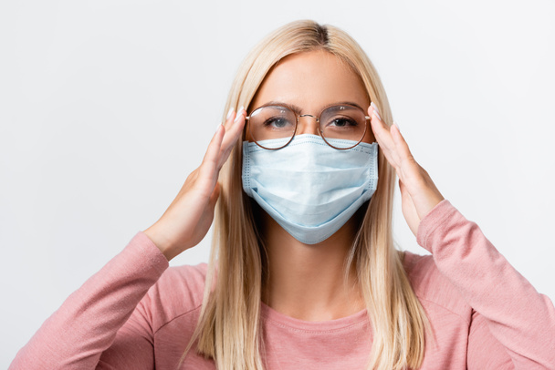 Young woman in medical mask touching eyeglasses isolated on grey - Photo, Image