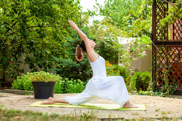 Jonge vrouw oefent yoga in de zomertuin - Warrior Pose, Virabhadrasana I. - Foto, afbeelding