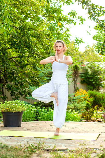 Young woman practices yoga in the summer garden - Vrikshasana, Tree Pose. - Photo, Image
