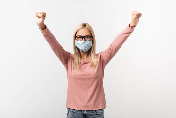 Woman in eyeglasses and medical mask showing yeah gesture isolated on grey - Foto, Imagem