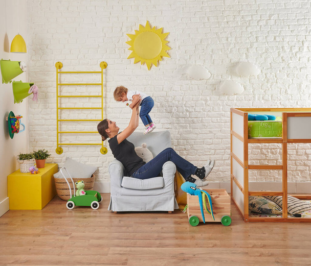 Μοντέρνο παιδικό δωμάτιο εσωτερικό στυλ, λευκό τούβλο τοίχο κίτρινο ήλιο και σύννεφο, πολυθρόνα, οικογένεια ψάχνει για παιδί και χαρούμενος. - Φωτογραφία, εικόνα