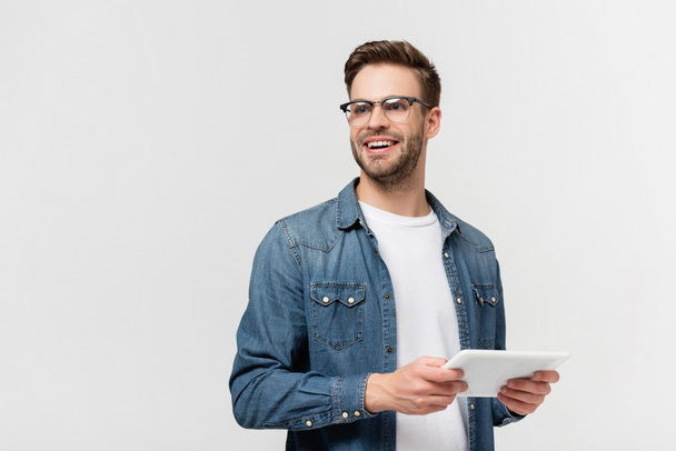 Hombre sonriente con gafas que sostiene la tableta digital aislada en gris - Foto, imagen