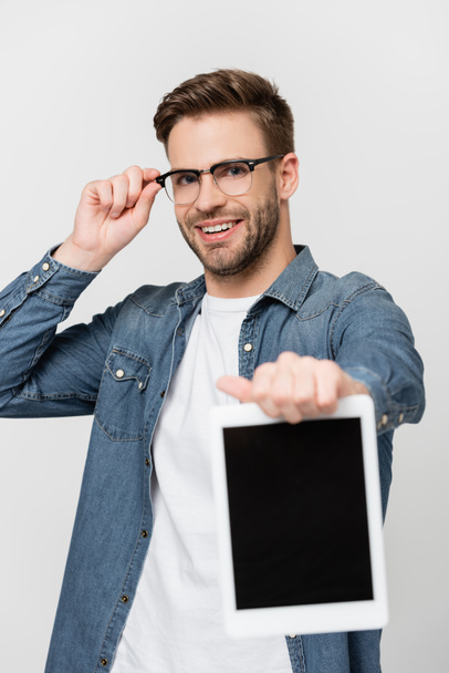 Uomo sorridente in occhiali che mostra tablet digitale con schermo bianco su primo piano sfocato isolato su grigio - Foto, immagini