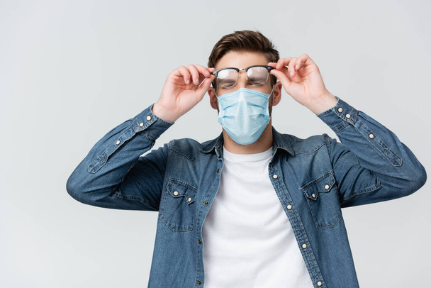 Young man in medical mask holding misted eyeglasses isolated on grey - Foto, imagen
