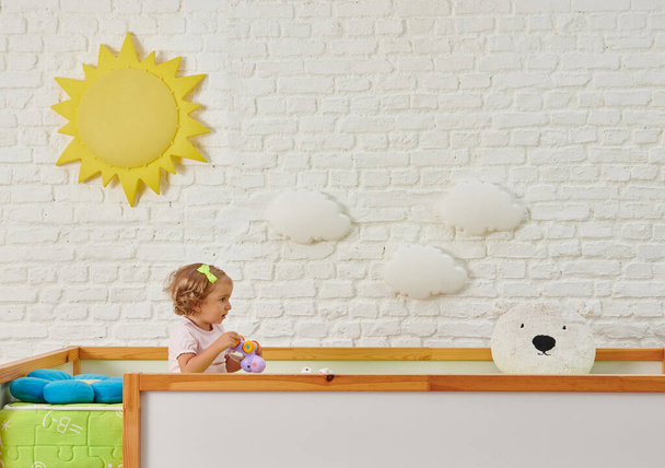 装飾的な木製のベビーベッドと子供のスタイル、白いレンガの壁の背景と太陽の雲のオブジェクトのインテリア. - 写真・画像