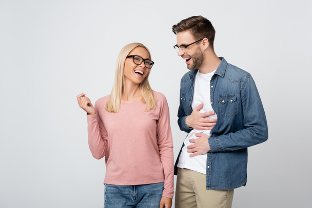 Young woman in eyeglasses standing near cheerful boyfriend isolated on grey - Фото, изображение