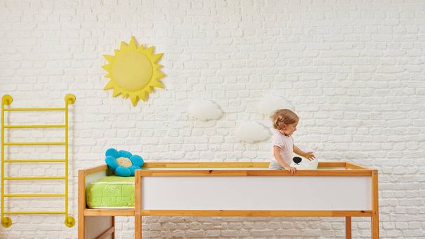 Koristeellinen puinen vauvan sänky ja lapsen tyyli, valkoinen tiiliseinä tausta ja aurinko pilvi esine sisustus. - Valokuva, kuva