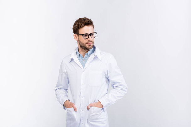 Silmälääkäri pitämällä kädet taskuissa valkoinen takki eristetty harmaa  - Valokuva, kuva