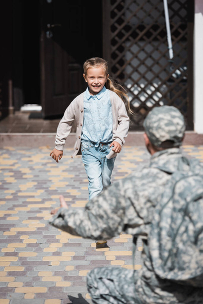 Szczęśliwa dziewczyna ucieka, z rozmytym ojcem w mundurze wojskowym na pierwszym planie - Zdjęcie, obraz