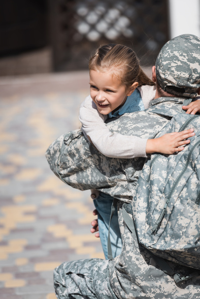 За поглядом військового, який обіймає усміхнену дочку на розмитому фоні. - Фото, зображення