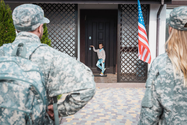 Girl standing on threshold with blurred military couple on foreground - Photo, Image