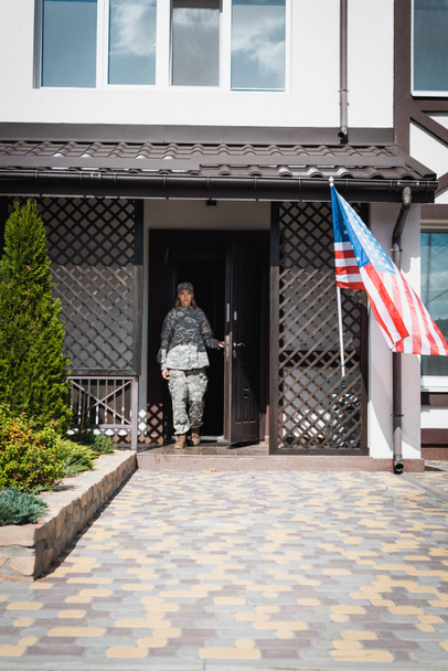 Militaire dienstbode in deuropening bij Amerikaanse vlag en struiken - Foto, afbeelding