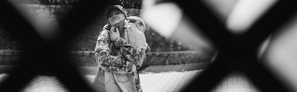 Happy mother in military uniform hugging daughter with blurred net on foreground, banner, monochrome - Photo, Image