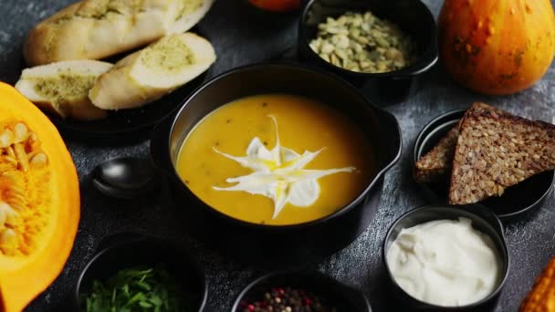 Deliziosa zuppa di zucca con panna, semi, pane ed erbe fresche in elegante ciotola nera in ceramica - Filmati, video