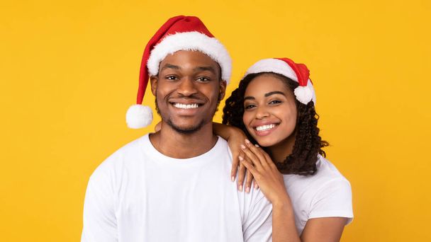 Kerst Portret van een zwart paar in Santa hoeden, gele achtergrond - Foto, afbeelding