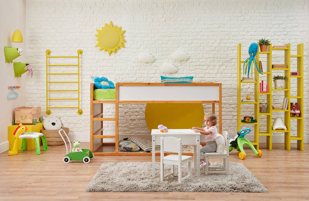 Moderne houten babykamer, kind, decoratieve trap en stapelbed, tafel en kind stijl. Speelgoed, witte bakstenen muur zon en wolk accessoire interieur. - Foto, afbeelding