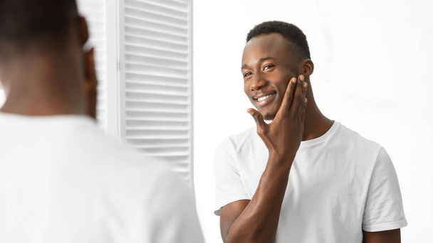 Guy Touching Shaved Face Looking In Mirror Standing In Bathroom - Photo, Image