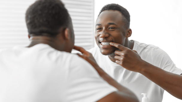 African Man Checking Teeth Smiling To Mirror Standing In Bathroom - Foto, Bild