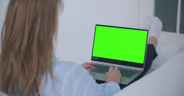 Eine junge Frau, die auf der Couch liegt, blickt auf den Bildschirm des Laptops mit grünem Bildschirm und nickt. Machen Sie einen Videoanruf - Filmmaterial, Video