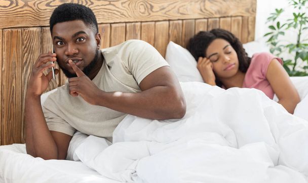 Μαύρος άντρας μιλάει με τον εραστή του στο κινητό στο κρεβάτι - Φωτογραφία, εικόνα