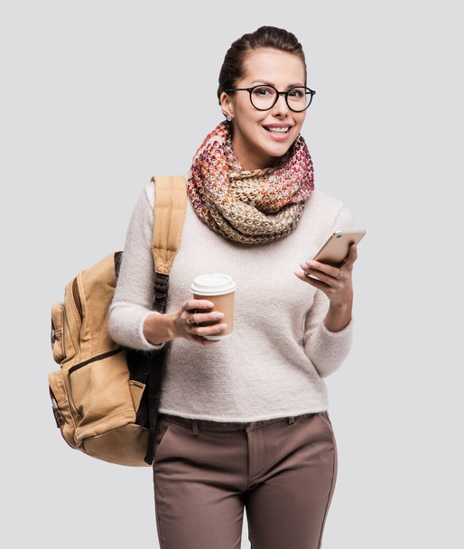Young surprised woman using smart phone. Student girl or traveler holding phone and coffee cup - Фото, зображення