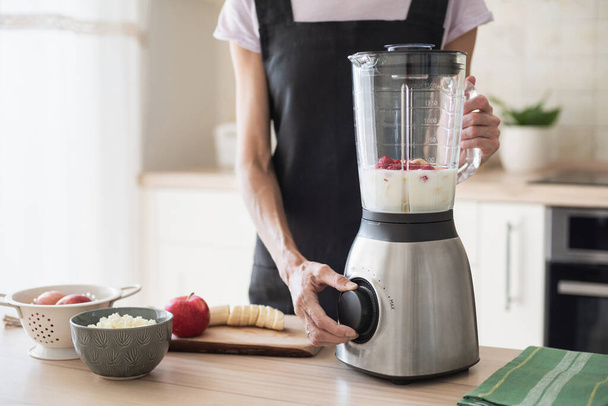 Young woman using a blender and cooking in the kitchen. Girl preparing smoothie and food at home. Healthy lifestyle and dieting concept - Foto, Imagen