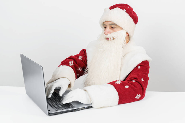 Christmas and New Year concept. Santa Claus sits at his desk and works at the computer. - Fotó, kép