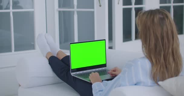 Una joven acostada en el sofá mira la pantalla del portátil con una pantalla verde y asiente con la cabeza. Hacer una videollamada - Imágenes, Vídeo