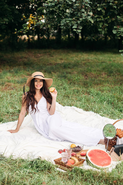 Портрет молодої красивої дівчини з навіть білими зубами, красива посмішка в солом'яному капелюсі і довга біла сукня мають пікнік в саду
 - Фото, зображення