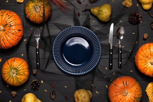 Autumn table setting with empty blue plate and pumpkins. Halloween or thanksgiving spooky tableware on dark wooden background - Photo, image